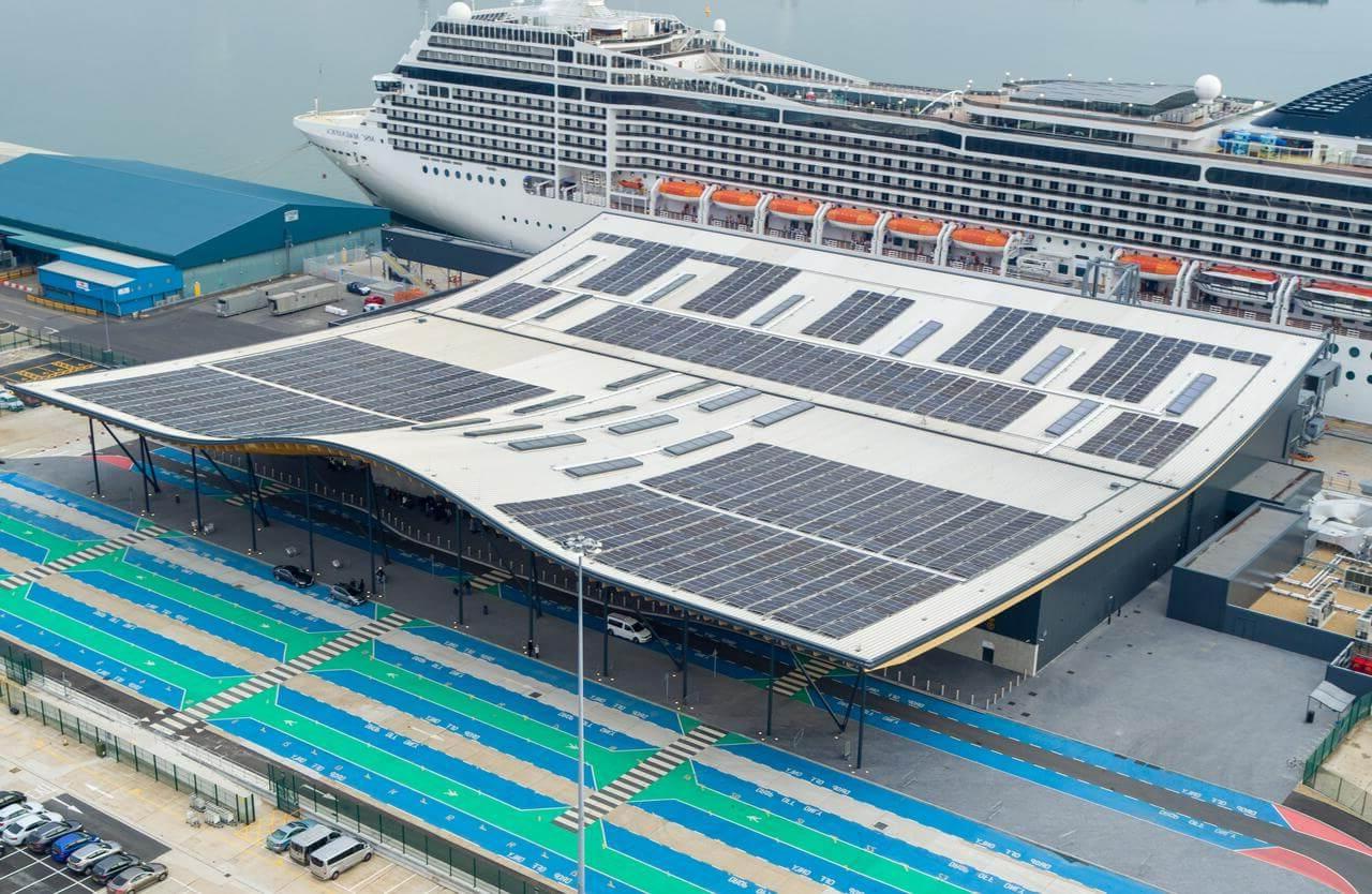 Solar panels on the roof of a cruise port terminal, with a cruise ship docked